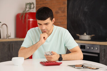 Young man counting money with calculator in kitchen