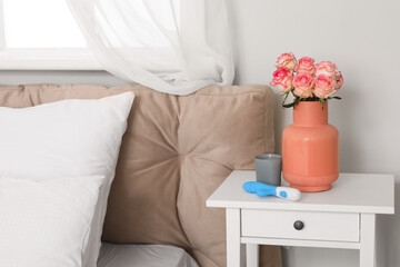 Vibrator and vase with roses on table in bedroom