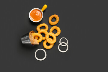 Metal bucket with fried breaded onion rings and sauce on black background