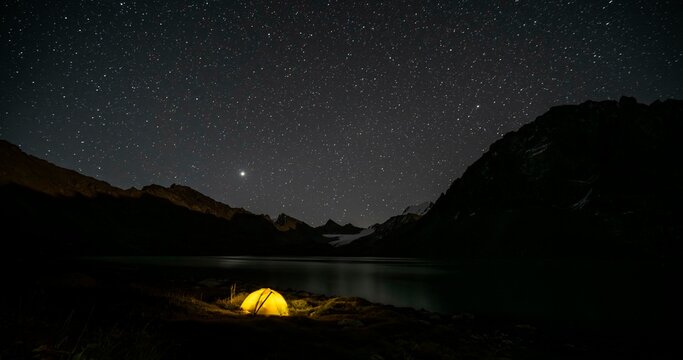 Yellow illuminated camping tent under a starry sky at the mountain lake Ala Kul Lake, mountain landscape at the lake at night, Ala Kul Lake, Tien Shan Mountains, Kyrgyzstan, Asia