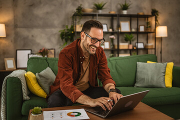 Adult happy caucasian man sit on sofa and work from home on lap top