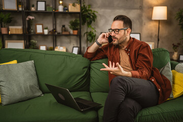 Adult caucasian man work from home on laptop and talk on mobile phone