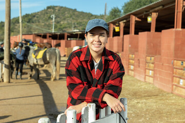 Portrait of young female stable worker smiling at camera during work in horse club on sunny spring...