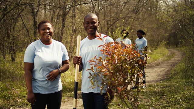 Portrait of african american couple fighting to preserve natural environment by planting trees, collecting rubbish and cultivating consciousness. Volunteers save the planet. Camera B. - Powered by Adobe