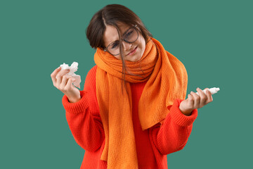 Sick little girl with tissue and nasal drops on green background