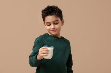 Cute little boy with glass of milk on beige background