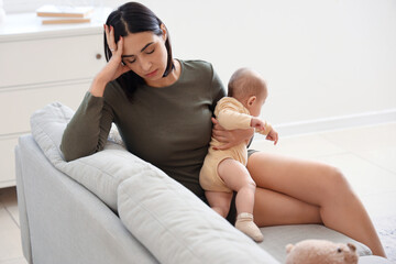 Young woman with her baby suffering from postnatal depression on sofa at home