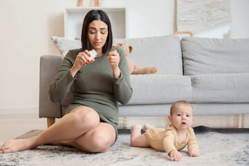 Young woman with pills and her baby suffering from postnatal depression at home