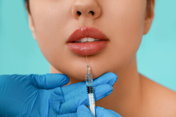 Young woman receiving lip injection on color background, closeup