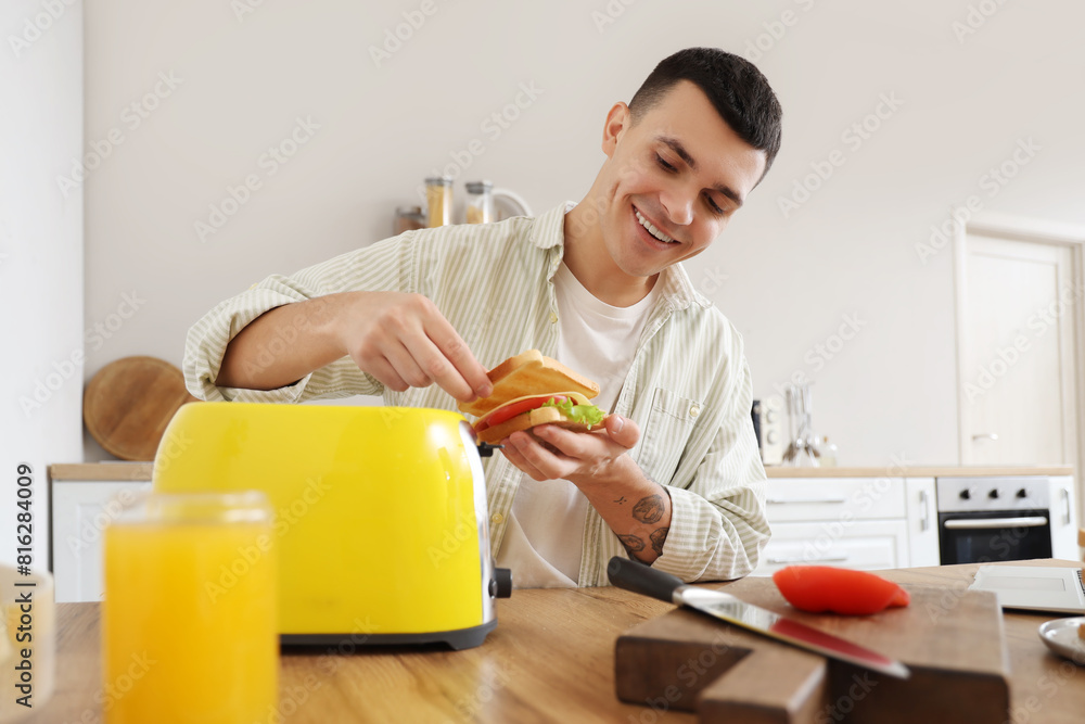 Canvas Prints Young man making tasty sandwiches from toasts in kitchen