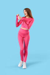 Sporty young woman with tasty yoghurt on blue background