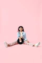 Young African-American woman in headphones with vinyl disk on pink background
