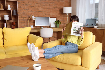 Young woman reading magazine in yellow armchair at home
