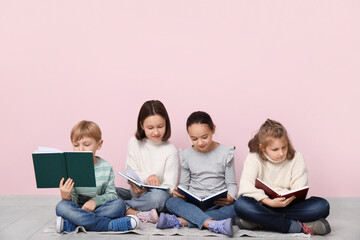 Little children reading books while sitting on floor near pink wall