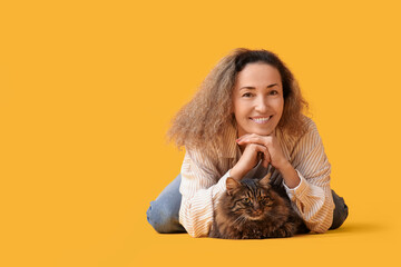 Mature woman with cute cat lying on yellow background
