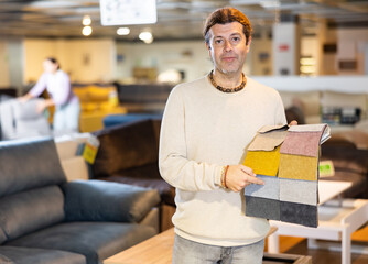 Middle-aged man shows upholstery fabric in the furniture shop