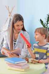 Fototapeta premium Mother and her son with different books sitting at table in children's room
