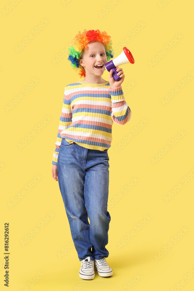 Poster Funny little girl in clown wig with megaphone on yellow background. April Fools' Day celebration