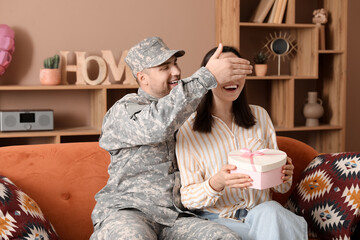 Man in military uniform covering eyes of his wife at home. Valentine's Day celebration