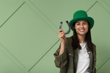 Beautiful young woman in leprechaun hat with horseshoe on green background. St. Patrick's Day...