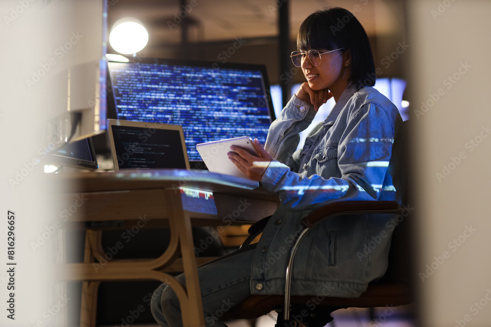 Poster female programmer working with tablet computer in office at night