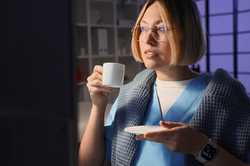 Female nurse with cup of coffee working evening shift in clinic, closeup