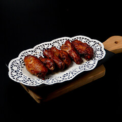 Grilled chicken wings on a black plate with white coasters.