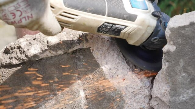 Close up of sparks flying from angle grinder disc cutter cutting through mild steel rebar in concrete block in slow motion