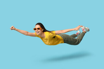 Joyful young woman in sunglasses flying on blue background