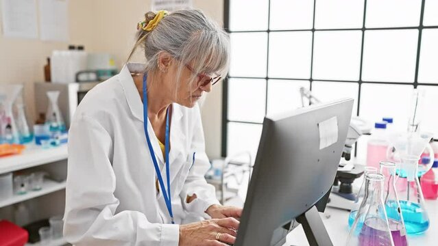 Mature woman scientist analyzing data on computer in laboratory