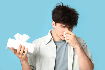 Young man with runny nose on blue background. Allergy concept