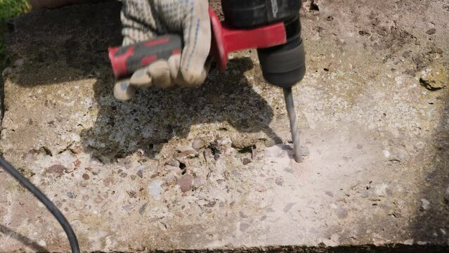 Close up of contractor drilling holes in concrete with an SDS hammer drill power tool to break up large concrete block into smaller pieces.
