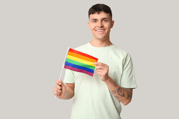 Handsome young happy man with LGBT flag on grey background