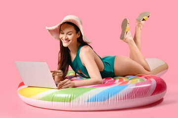 Smiling woman with laptop lying on inflatable mattress against pink background