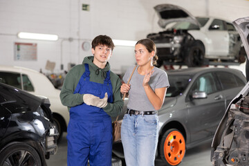 Young guy mechanic advises young woman client on car repair in car service station..