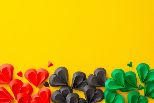 Bright red, green, and black paper hearts arranged creatively on a yellow backdrop, symbolizing unity and freedom in celebration of Juneteenth