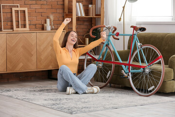 Happy young woman with gift bicycle sitting at home