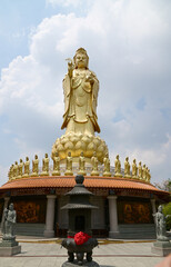 Fototapeta premium BANGKOK, THAILAND - May 16, 2024: A large golden statue of the Goddess Kuan Yin Set tall and elegant and small statues of the Goddess Kuan Yin decorated around with blue sky background.