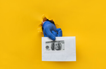 The male hand in a blue fabric work glove holds an envelope with dollar bills (money). Torn hole in...