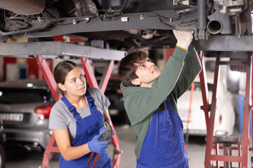 Experienced auto mechanic tells a novice auto mechanic how to properly repair a car at a car...