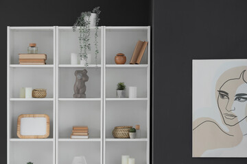 Shelf unit with blank frame, books and decor near dark wall in room