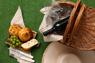 Wicker picnic basket with tasty food, glasses and bottle of wine on green grass background