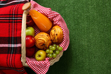 Wicker picnic basket with tasty food and bottle juice on green grass background