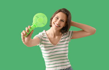 Young woman with small electric fan on green background