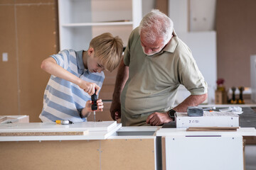 A grandfather teaches his grandson how to fix furniture in his carpenter workshop. They work...