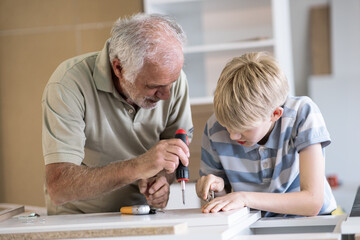 A grandfather teaches his grandson how to fix furniture in his carpenter workshop. They work together, sharing tools and skills, as the grandfather passes on his knowledge.