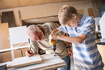 A grandfather teaches his grandson how to fix furniture in his carpenter workshop. They work...