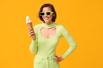 Beautiful young woman in sunglasses with sweet ice-cream in waffle cone on yellow background