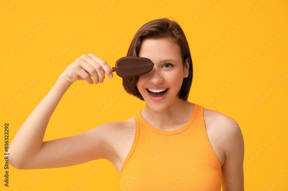 Poster Beautiful young woman with chocolate covered sweet ice-cream on yellow background