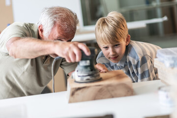A grandfather teaches his grandson how to fix furniture in his carpenter workshop. They work...